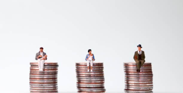 An equal pay concept. Miniature people sitting in the same height pile of coins. stock photo