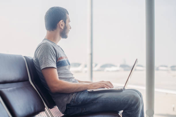istock Young man using laptop in airport terminal 953445882