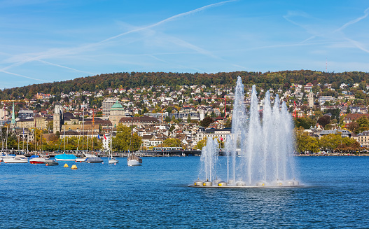 A fountain and boats on Lake Zurich in Switzerland, buildings of the city of Zurich in the background. The picture was taken at the beginning of October.
