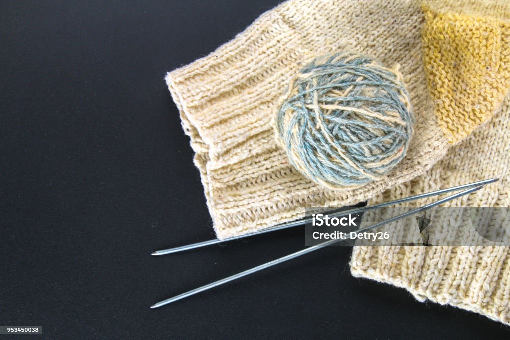A ball of wool with knitting needles and socks on a gray table. Needlework. A ball of wool with knitting needles and socks on a gray table. Needlework Art And Craft Stock Photo
