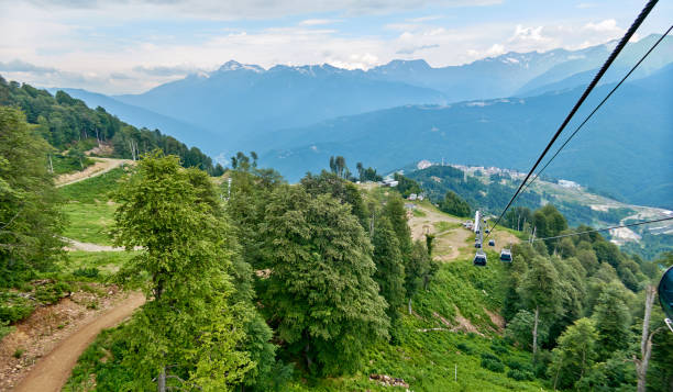 camino soleado teleférico en sochi en rosa khutor bajo cielo azul con verde bosque - overhead cable car summer ski lift scenics fotografías e imágenes de stock