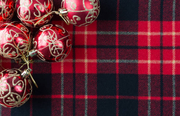 Top view of several Christmas ornaments atop a red, black and white tartan cloth with room for a message.
