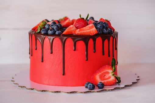 beautiful home made bright red cake with strawberry and blueberry berries, chocolate frosting on white table