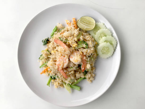 istock Fried rice with prawn herbs and vegetables served with lemon and cucumber in white plate on white background. Part of a series of nine Asian food dishes. Thai Food. 953459444