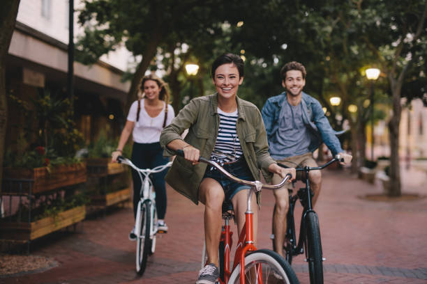 Young friends cycling in the city Three young people cycling down the street. Male and female friends on road with their bikes. riding photos stock pictures, royalty-free photos & images