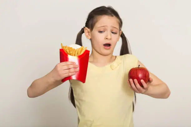 Photo of Hesitated little girl holding a bag of fries and apple