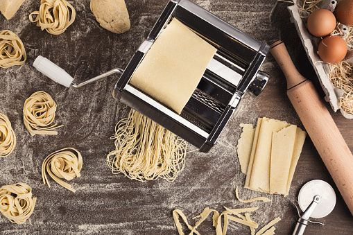 Preparing homemade fettuccine on pasta machine. Top view on raw tagliatelle nests and special equipment for making traditional Italian meal, copy space