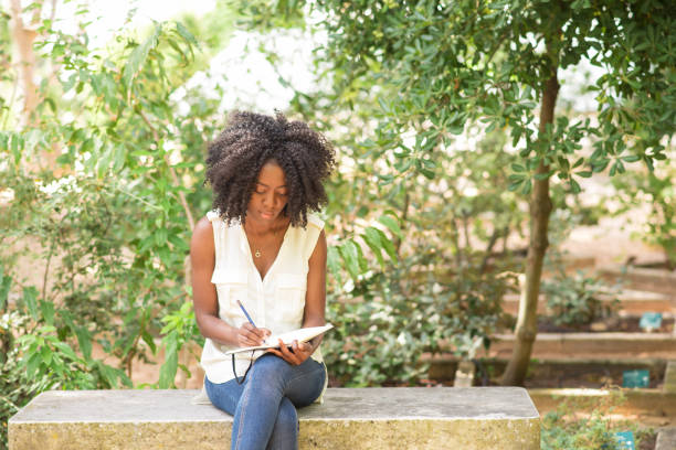 Focused young attractive black woman making notes in park