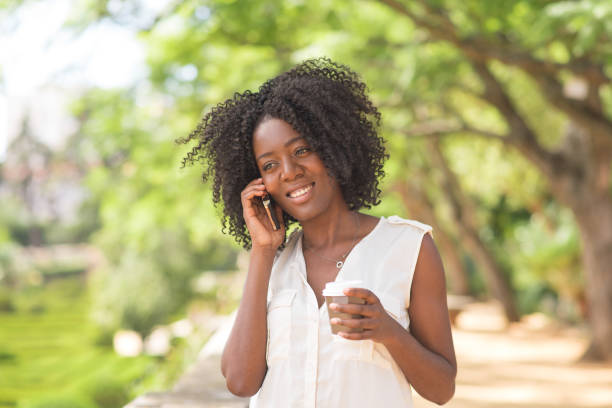 istock Smiling young black woman drinking coffee and calling on phone 953512000