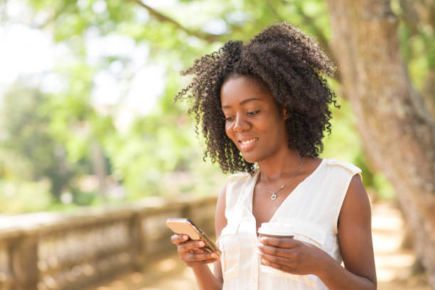 istock Smiling pretty black woman drinking and using smartphone in park 953512062