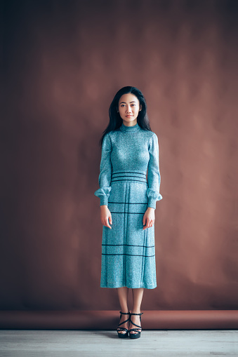 Full length portrait of beautiful asian girl in blue dress on brown background posing in studio