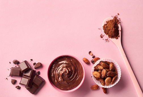Dark chocolate, cacao powder and beans on pink background. Top view
