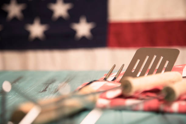 istock Outdoor grilling, BBQ utensils on rustic picnic table with USA flag. 953513660