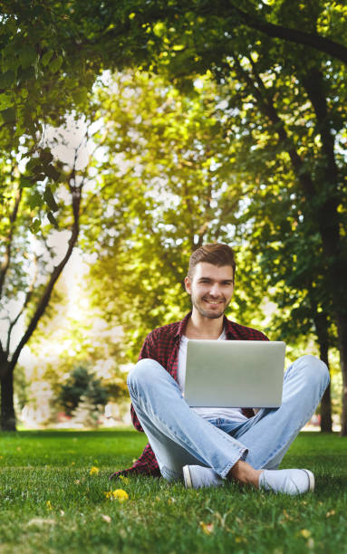 istock Happy man is sitting in the park and using laptop 953521412