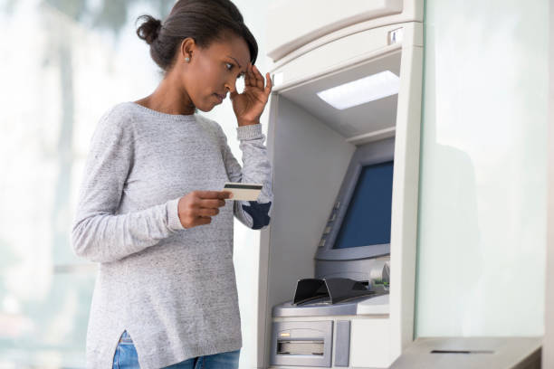 Woman with a headache holding hand on forehead, having financial problems to withdraw cash from an ATM machine. Sad, worried woman with the hand on her forehead had problems with a credit card to withdraw cash from an ATM machine. exchange teller stock pictures, royalty-free photos & images