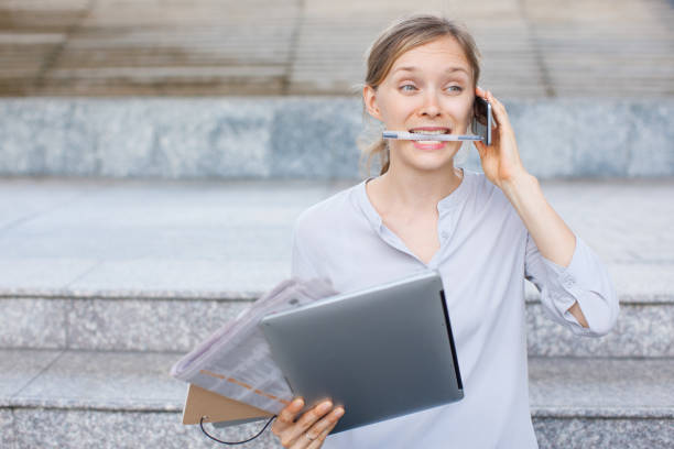 Multitasking businesswoman talking on phone with pen in teeth
