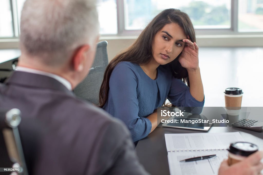 Business leader instructing serious Indian female assistant Business leader instructing focused Indian female assistant. Serious and upset woman leaning head on hand and listening to boss during coffee break. Teamwork or company hierarchy concept Displeased Stock Photo