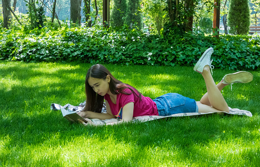 young girl reading a book in a picturesque park, sunny day. the girl of Asian appearance
