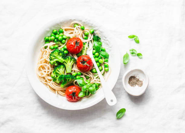 istock Simple veggie pasta. Vegetarian pasta spaghetti with broccoli cabbage, green peas and cherry tomatoes on light background, top view 953533746