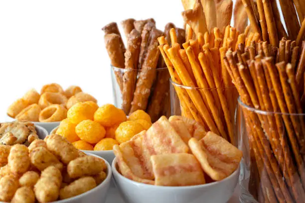 Selection of many types of savory snacks in white ceramic dishes and glasses.