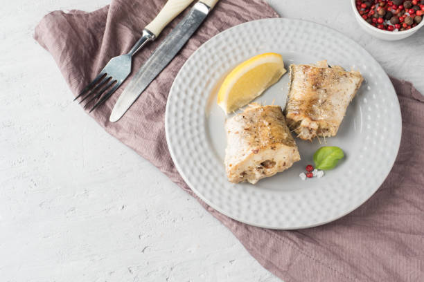 baked pollock fish with lemon and spices on a plate napkin on the table - pollock trawler imagens e fotografias de stock