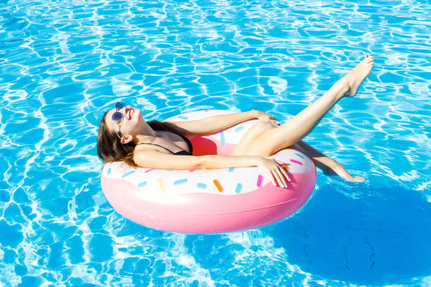 piękna młoda kobieta z różowym kółkiem relaksującym się w niebieskim basenie - swimming tube inflatable circle zdjęcia i obrazy z banku zdjęć