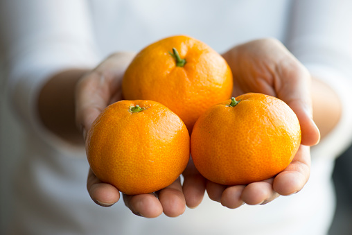 Tangerines on a plate on a brown rustic wooden table. Female hands. Top view of fresh mandarins.