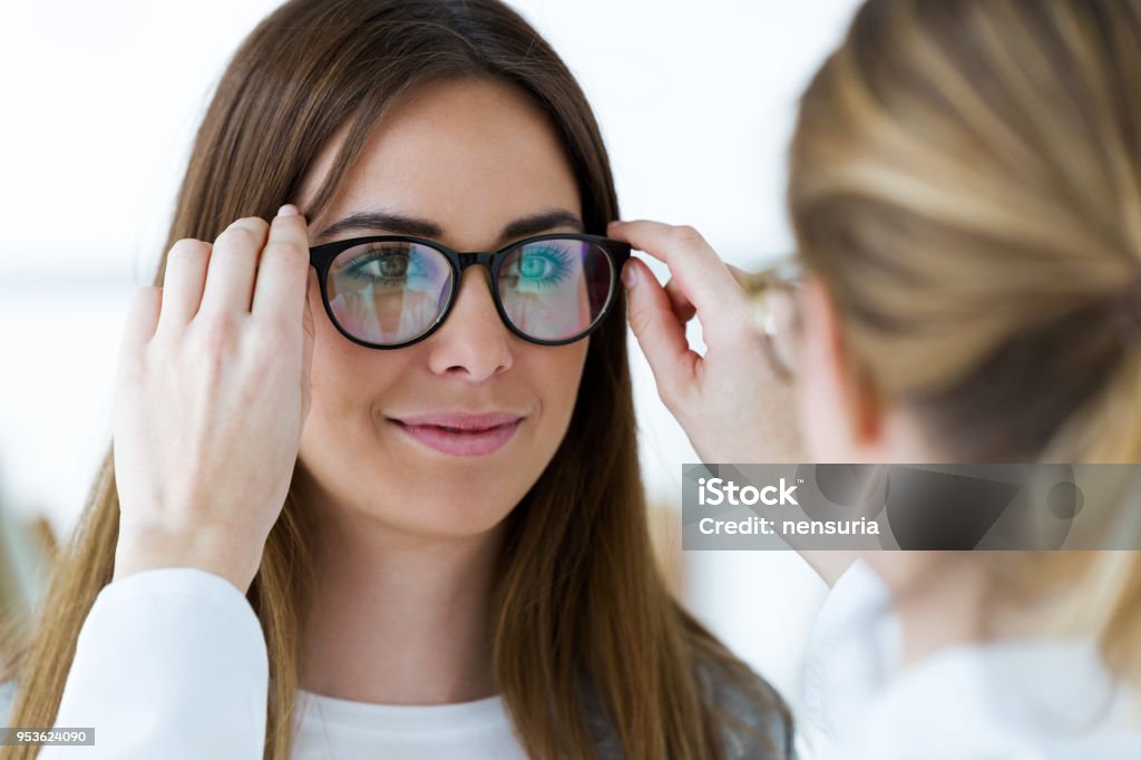 Optometrist and pretty young woman choosing eyeglasses in optics. Close-up of optometrist and pretty young woman choosing eyeglasses in optics. Eyeglasses Stock Photo