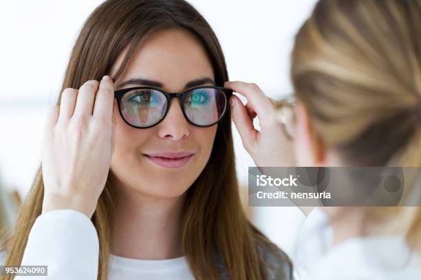 Optometrist And Pretty Young Woman Choosing Eyeglasses In Optics Stock Photo - Download Image Now