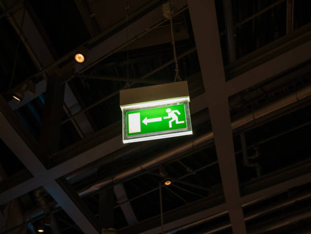 освещенный зеленый знак выхода в темной комнате - people metal sign way out sign стоковые фото и изображения