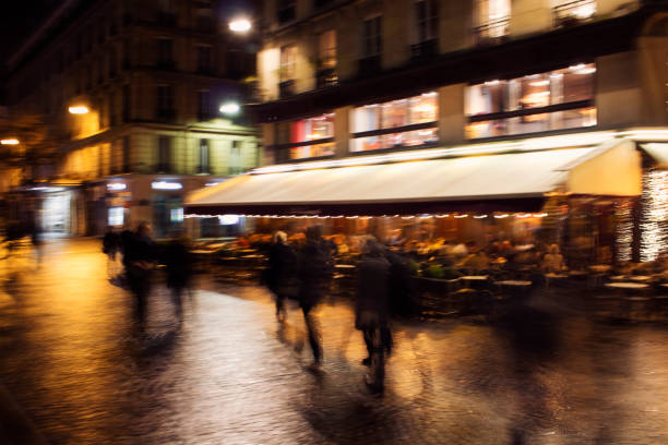 Blurry motion image of people walking on street at night in Paris.