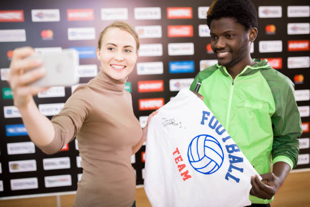 Football Player Posing for Selfie with Fan Portrait of smiling African-American sportsman taking selfie with fan and holding signed t-shirt celebrity fans stock pictures, royalty-free photos & images