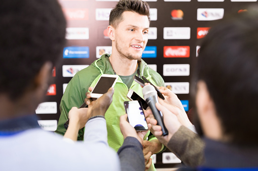 Portrait of handsome young sportsman giving interview to group of journalists during press conference