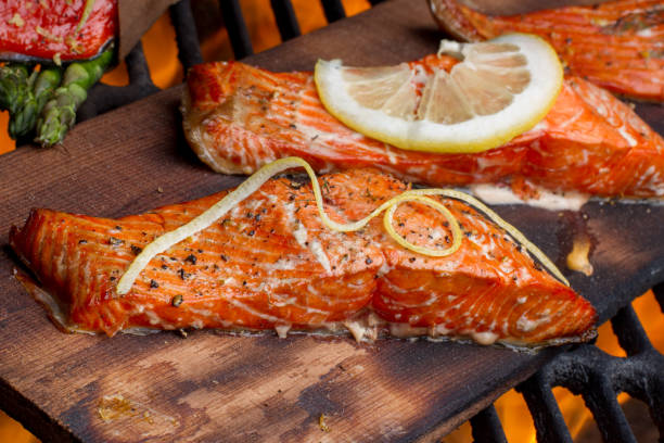 Wild Caught Salmon on a Grill Wild caught king salmon filets topped with lemon slices and dill weed and coarse ground black pepper on top of a cedar plank on an old fashioned charcoal grill fully cooked and ready to be served. goodfood stock pictures, royalty-free photos & images