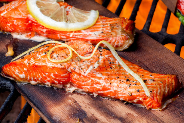 Wild Caught Salmon on a Grill Wild caught king salmon filets topped with lemon slices and dill weed and coarse ground black pepper on top of a cedar plank on an old fashioned charcoal grill fully cooked and ready to be served. goodfood stock pictures, royalty-free photos & images