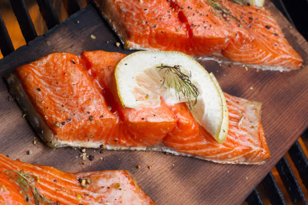 Wild Caught Salmon on a Grill Wild caught king salmon filets topped with lemon slices and dill weed and coarse ground black pepper on top of a cedar plank on an old fashioned charcoal grill fully cooked and ready to be served. goodfood stock pictures, royalty-free photos & images