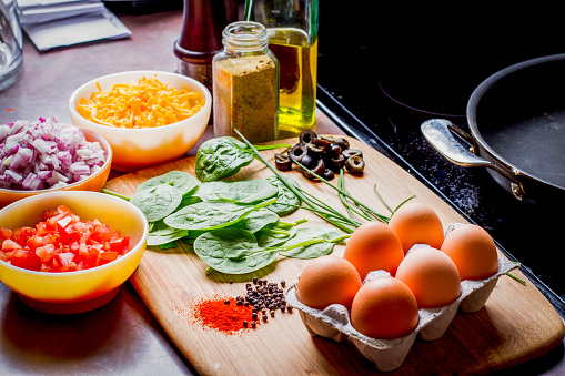 Eggs, cheese, spinach, onion, olives, tomato and seasoningson a bamboo cutting board,, the ingredients for a perfect ketogenic diet healthy breakfast.