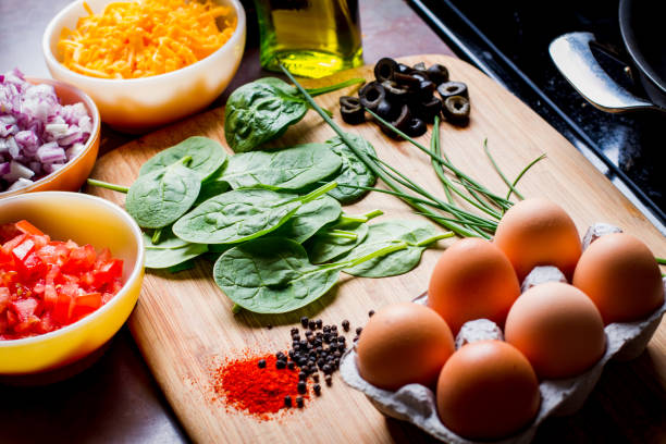 Making the Perfect Low Carb Omelette Eggs, cheese, spinach, onion, olives, tomato and seasoningson a bamboo cutting board,, the ingredients for a perfect ketogenic diet healthy breakfast. goodfood stock pictures, royalty-free photos & images