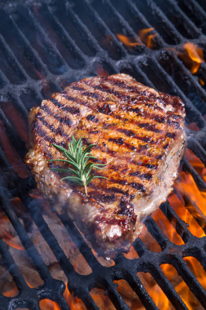 High Fat Low Carb Grilled Rib Eye Beef Steak Low Carb, high fat big gourmet rib eye beef steak with a sprig of rosemary on a flaming grill.  Grass-fed beef is a staple of the ketogenic diet goodfood stock pictures, royalty-free photos & images