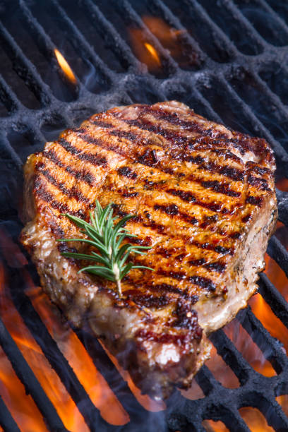 High Fat Low Carb Grilled Rib Eye Beef Steak Low Carb, high fat big gourmet rib eye beef steak with a sprig of rosemary on a flaming grill.  Grass-fed beef is a staple of the ketogenic diet goodfood stock pictures, royalty-free photos & images