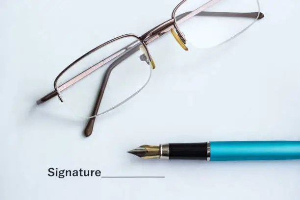 Document for signing beside glasses and pen, close-up