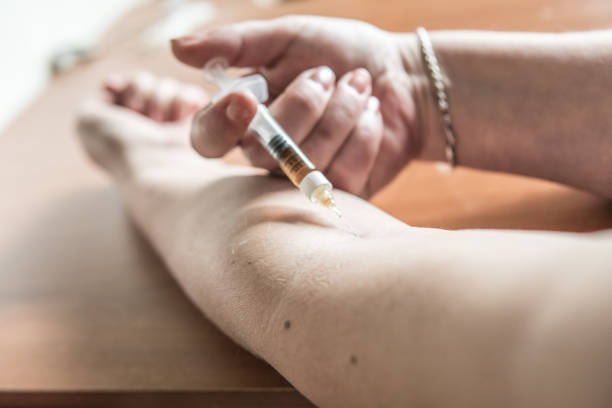 Woman puts a syringe in the arm with medicine or illegal drugs. stock photo
