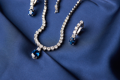 Close-up of women's platinum necklace and earrings with a diamond and blue precious sapphire stone . Luxury female jewelry