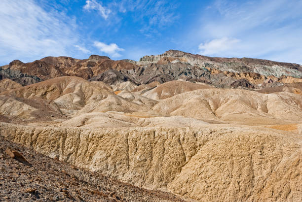 Twenty Mule Team Canyon The colorful landscape seen at Zabriskie Point extends several miles to the southeast. These spectacular multi-colored "badlands" formations may be viewed close up in Twenty Mule Team Canyon, a dry wash that winds through the undulating hills. The eroded formations have greatly contrasting colors - black or dark brown to the west, cream, yellow and white to the east. Zabriskie Point and Twenty Mule Team Canyon are in Death Valley National Park, California, USA. jeff goulden badlands stock pictures, royalty-free photos & images