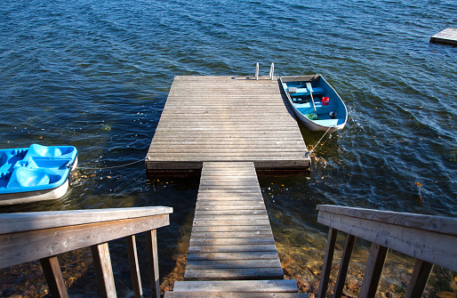Paddle boat and fishing boat tied to a wooden lakeside dock with staircase