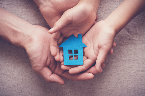 Adult and child hands holding paper house, family home and homeless shelter concept