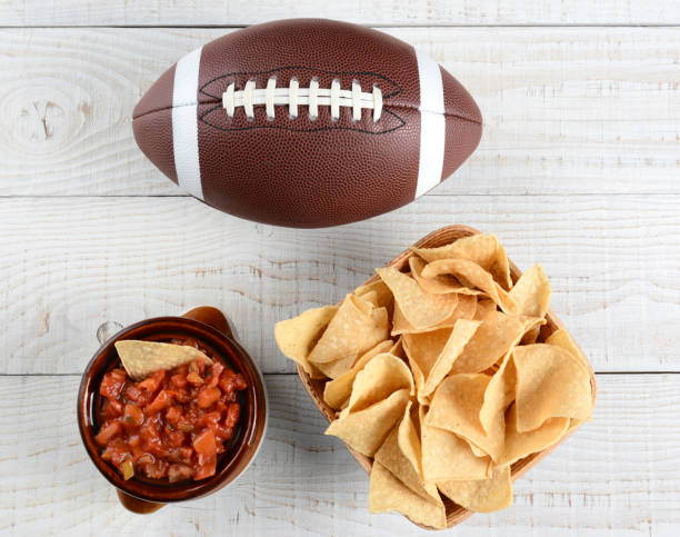 Chips, Salsa and Football High angle shot of a bowl of corn chips a crock full of fresh salsa and an American football on a whitewashed rustic wood table. Horizontal format. pigskin stock pictures, royalty-free photos & images