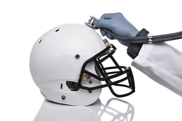 Football Concussion Concept A football helmet and doctors hand holding a stethoscope on the crown of the helmet. Sports Concussion Concept, and related conditions, CTE, Alzheimer's, Parkinson's. brain damage stock pictures, royalty-free photos & images