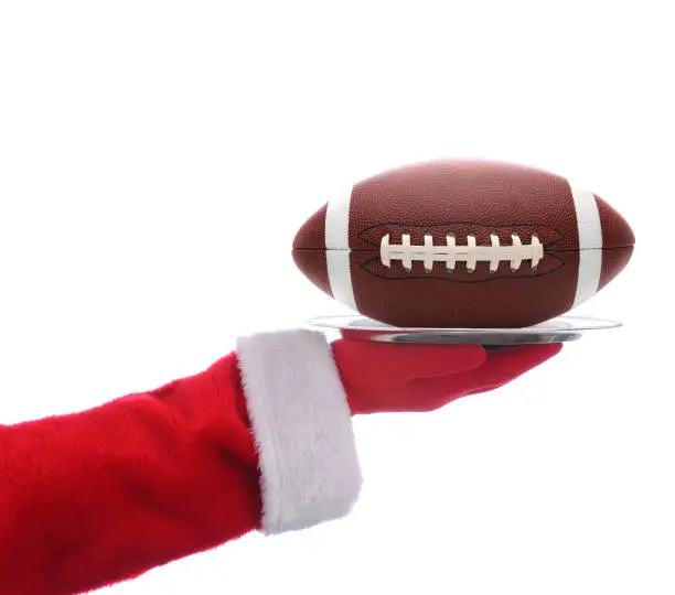 Santa Claus outstretched arm holding an American Football on a serving tray. Horizontal format over a white background.