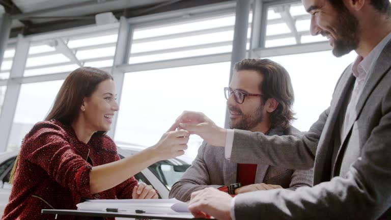 Couple customer receiving car keys and handshaking with couple customers in car dealership